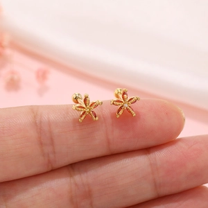 Macro view of tiny gold starfish earrings with reddish gems held on a fingertip