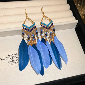 Detail of blue feather bohemian earrings with enamel diamond-shaped accents and gold chains