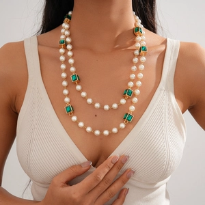 Detail of a layered necklace with white imitation pearls and green emerald-style gemstones