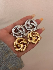 Detailed view of knotted gold and silver earrings held in hand for size perspective