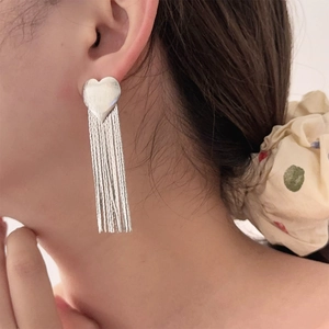 Detail shot of heart-shaped tassel earrings with brushed silver finish on a model