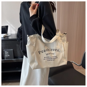 Detailed shot of large cream canvas tote bag with side pockets and black lettering design