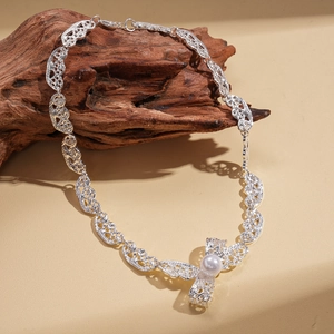 Detail of silver bow pendant with faux pearl on hollow pattern chain over dark wood