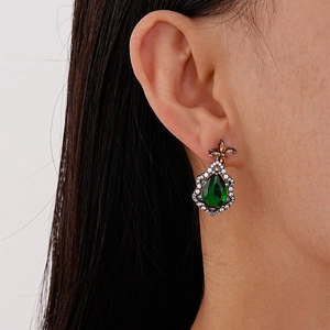 Vintage teardrop earrings with green gems and floral studs on a female model