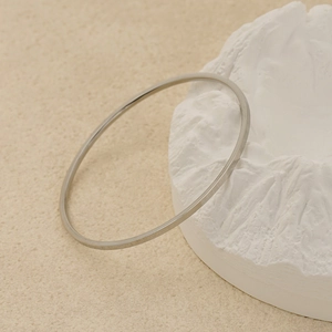 Bracelet plat minimaliste en acier argenté sur support décoratif de montagne blanche