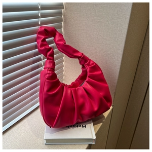 Detail of fuchsia pleated shoulder bag with twisted soft leather handle on a prop book
