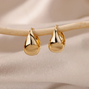 Macro shot of gold teardrop earrings hanging on a natural wooden branch with satin background