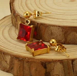 Detail of gold zircon earrings with square red gemstones on a natural wood surface