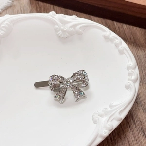 Close-up of a silver Y2K bow hair clip with sparkling rhinestones on a ceramic tray