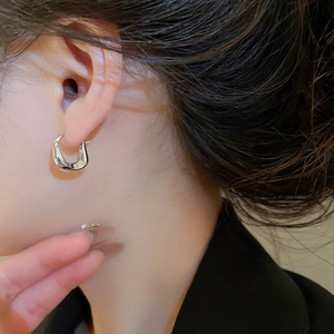 Close-up of minimalist silver twisted U-shaped hoop earring worn by a female model
