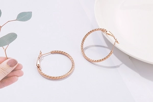 Detailed close-up of rose gold hoop earrings featuring elegant spiral texture on white ceramic