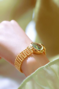 Close-up of luxury gold-tone metal strap and green dial watch with soft blurred background