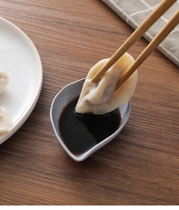 Close-up of dumplings being dipped into a grey heart-shaped sauce dish on a wooden table