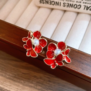 Detailed close-up of red floral and butterfly tassel earrings with pearls on a wooden stand
