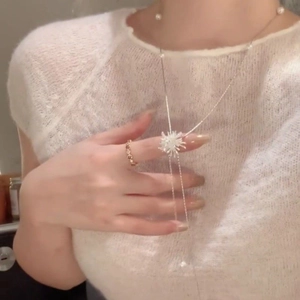 Détail du collier pendentif étoile avec longues pampilles et perles sur pull en maille blanc