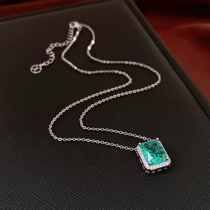 Detailed view of silver necklace with emerald-cut green gemstone in halo setting on display