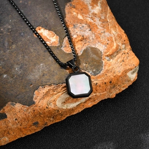 Detailed view of square link chain and octagonal pendant with white shell inlay on a rock