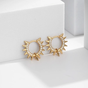Gold spiked huggie hoop earrings with sparkling cubic zirconia on white stone pedestal