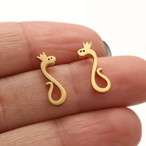 Golden cartoon snake stud earrings with crown detail held by fingers on plain background