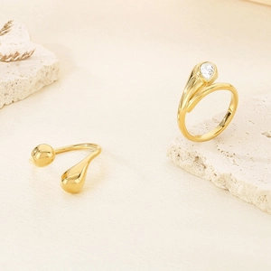Polished gold water drop open ring and pear cut gemstone ring on a natural stone base