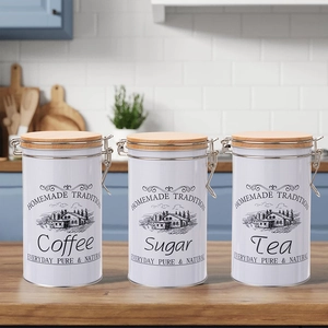 Three white tin coffee sugar tea canisters with wood lids and metal clasps on a kitchen counter