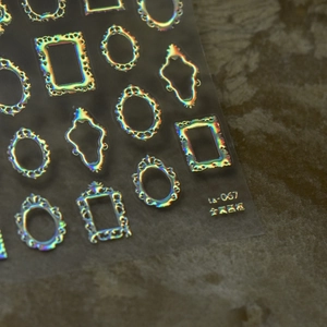 Macro detail of holographic gold picture frame nail stickers on a textured rock surface
