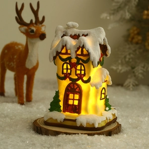 Close-up of a glowing Christmas house with snowy roof and warm light on wooden base