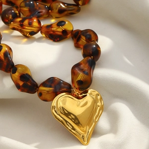 Macro shot of amber leopard resin beads and hammered gold heart pendant on a silk background