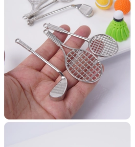 Detailed close-up of a mini silver metal tennis racket and golf club miniature set
