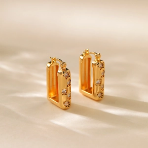 Close-up of gold-plated rectangular huggie earrings with zircon star design in warm light