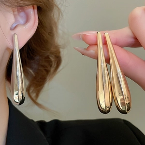 Detailed close-up of teardrop earrings in polished gold and silver finishes on a model