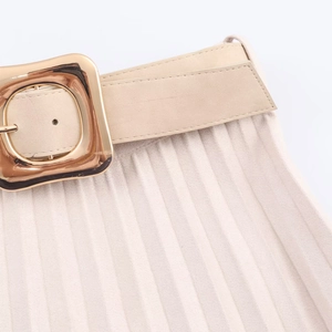Détail d'une jupe plissée beige avec ceinture assortie et boucle métallique carrée dorée