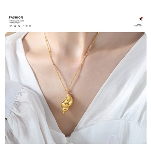 Close-up of a gold conch pendant necklace with small bead chain on a female model