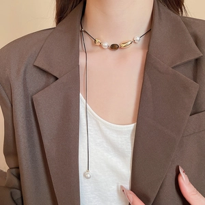 Close-up of tiger eye stone and pearl flower pendant necklace on model with brown blazer