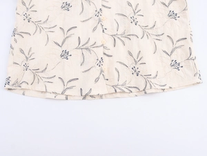 Detailed close-up of dark floral embroidery and linen texture on a beige V-neck blouse