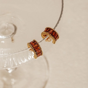 Macro detail of gold earrings with amber zircons and bead edges on a glass rim
