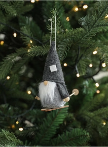 Detail of gray plush Christmas gnome with wooden skis hanging on a lit Christmas tree