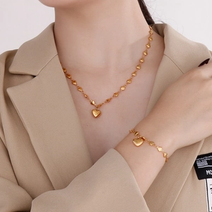 Detail of gold heart pendant necklace and matching bracelet on a chic khaki blazer