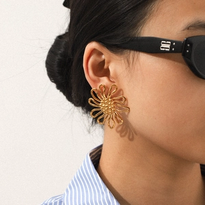 Close-up of elegant gold flower stud earrings worn by a model in a minimalist style