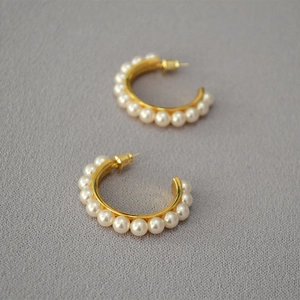 Macro shot of elegant gold-plated C-shaped earrings with multiple round pearls