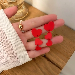Close-up of red flocked heart earrings held by a model with a vintage matte finish