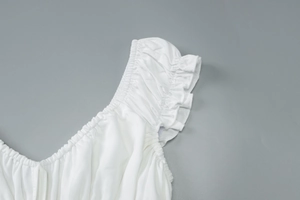 Détail de robe blanche montrant le décolleté en V plissé et les manches à volants