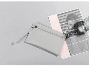 Close-up of minimalist gray leather clutch bag with matching wristlet strap on a magazine