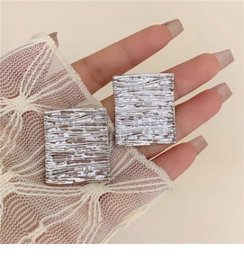 Detailed macro view of silver geometric square earrings with textured brushed metal finish
