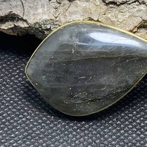 Dettaglio macro del ciondolo in labradorite a goccia con bordo dorato su legno rustico