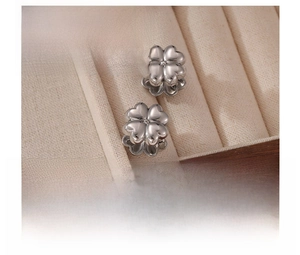 Macro detail of silver four-leaf clover titanium steel earrings in a beige velvet jewelry box