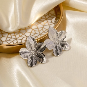 Macro shot of silver flower stud earrings with radial texture on cream satin fabric