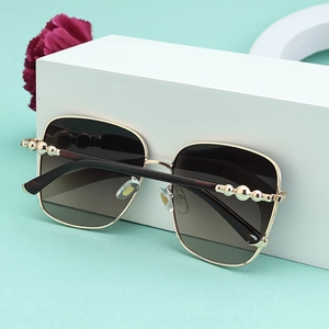 Detailaufnahme der quadratischen Gold-Sonnenbrille mit braunen Verlaufsgläsern auf weißen Blöcken