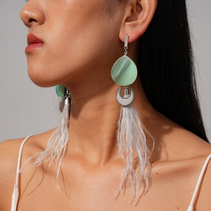 Detailed view of long tassel earrings with green resin drop and white feather fringe