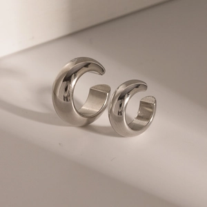 Detail of silver C-shaped ear cuffs on a beige surface showing minimalist metallic texture